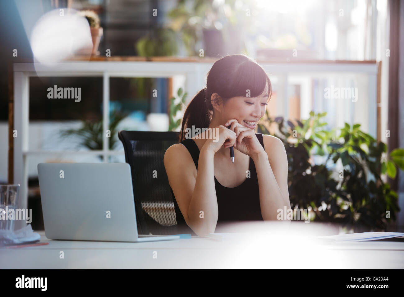 Shot of young woman sitting at office desk looking at documents and smiling. Asian business woman going through paperwork at her Stock Photo