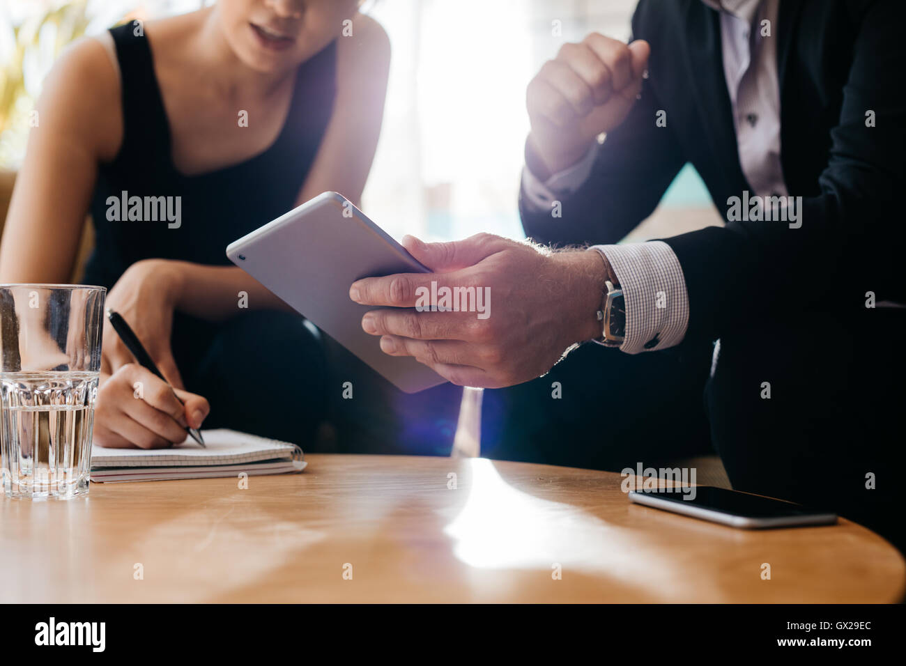 Business colleagues working together in office, focus on man using electronic organizer in foreground and woman writing notes. Stock Photo