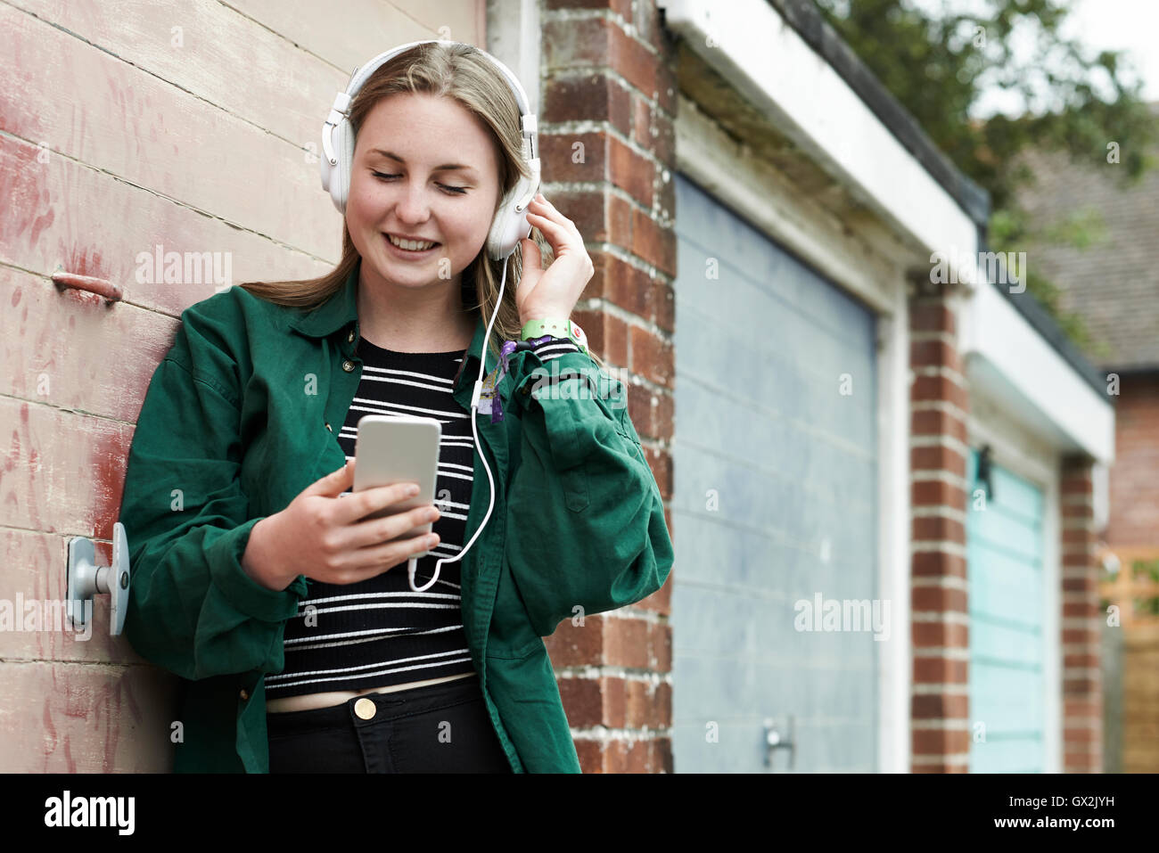 Teenage Girl Wearing Headphones And Listening To Music In Urban Setting Stock Photo