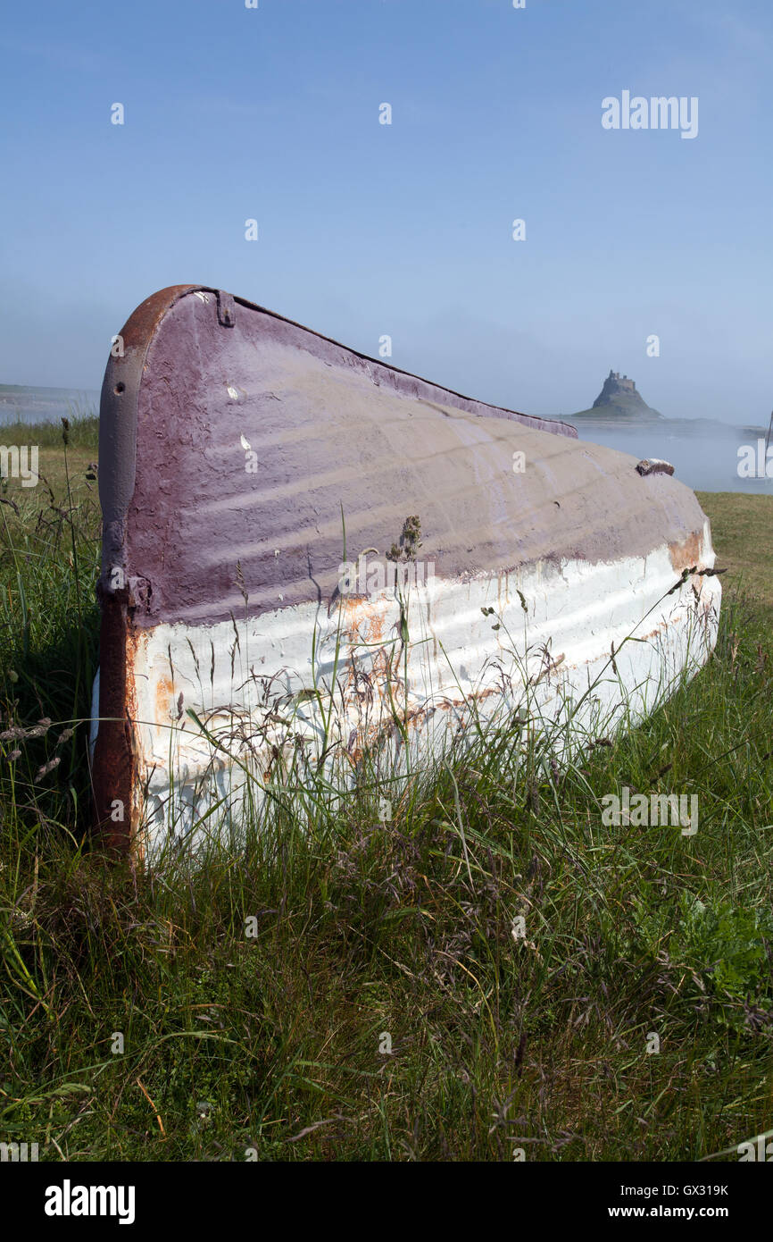 Upturned fishing boat on the beach at Holy Island with Lindisfarne Castle in the background Northumberland England UK Stock Photo