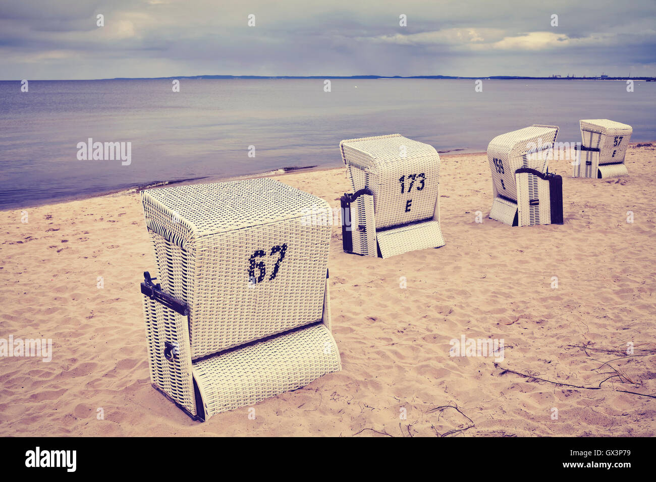 Vintage toned hooded wicker basket chairs on an empty beach. Stock Photo