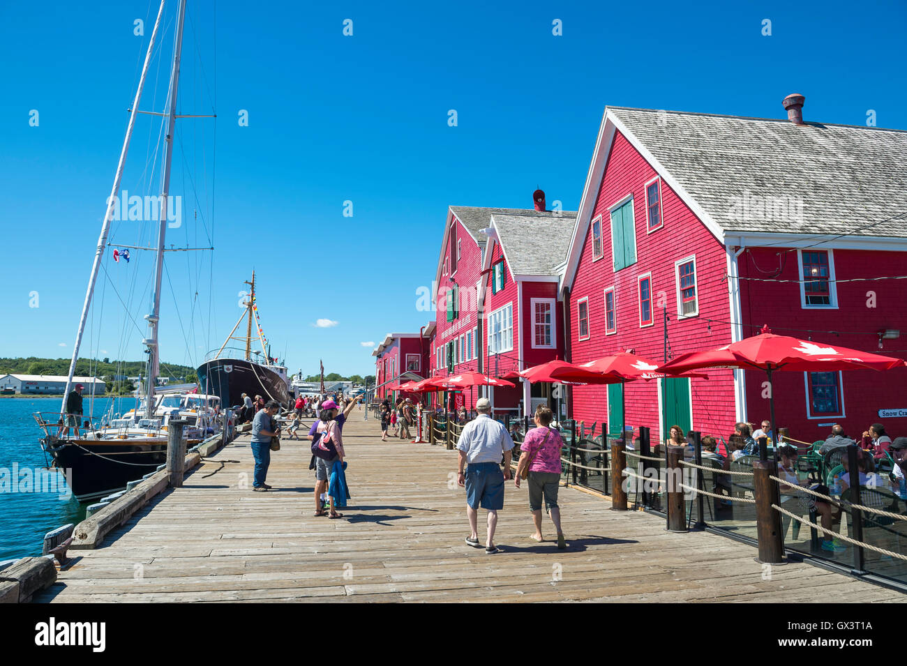 LUNENBURG, NOVA SCOTIA - AUGUST 23, 2016: Tourists stroll along the rustic wooden boardwalk in front of the classic architecture Stock Photo