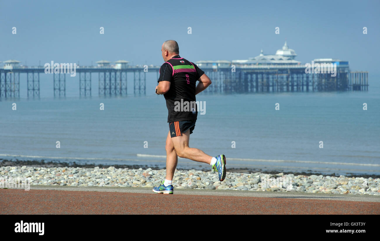RUNNER RUNNING PAST THE PIER AT LLANDUDNO NORTH WALES RE HEALTH FITNESS EXERCISE FIT ELDERLY RETIREMENT PENSIONERS SEASIDE UK Stock Photo