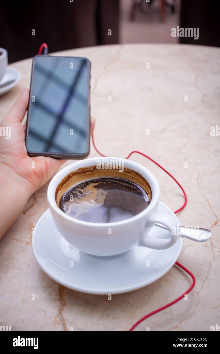 Smartphone at hand and americano coffee in white cup at marble table top Stock Photo