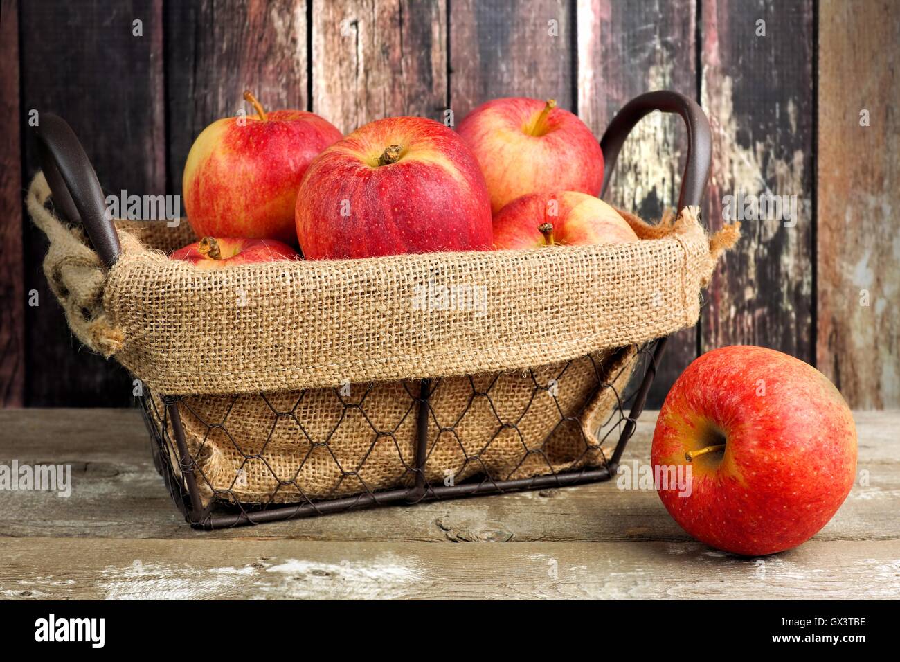 Fresh apples in a vintage wire basket with burlap against rustic wood background Stock Photo