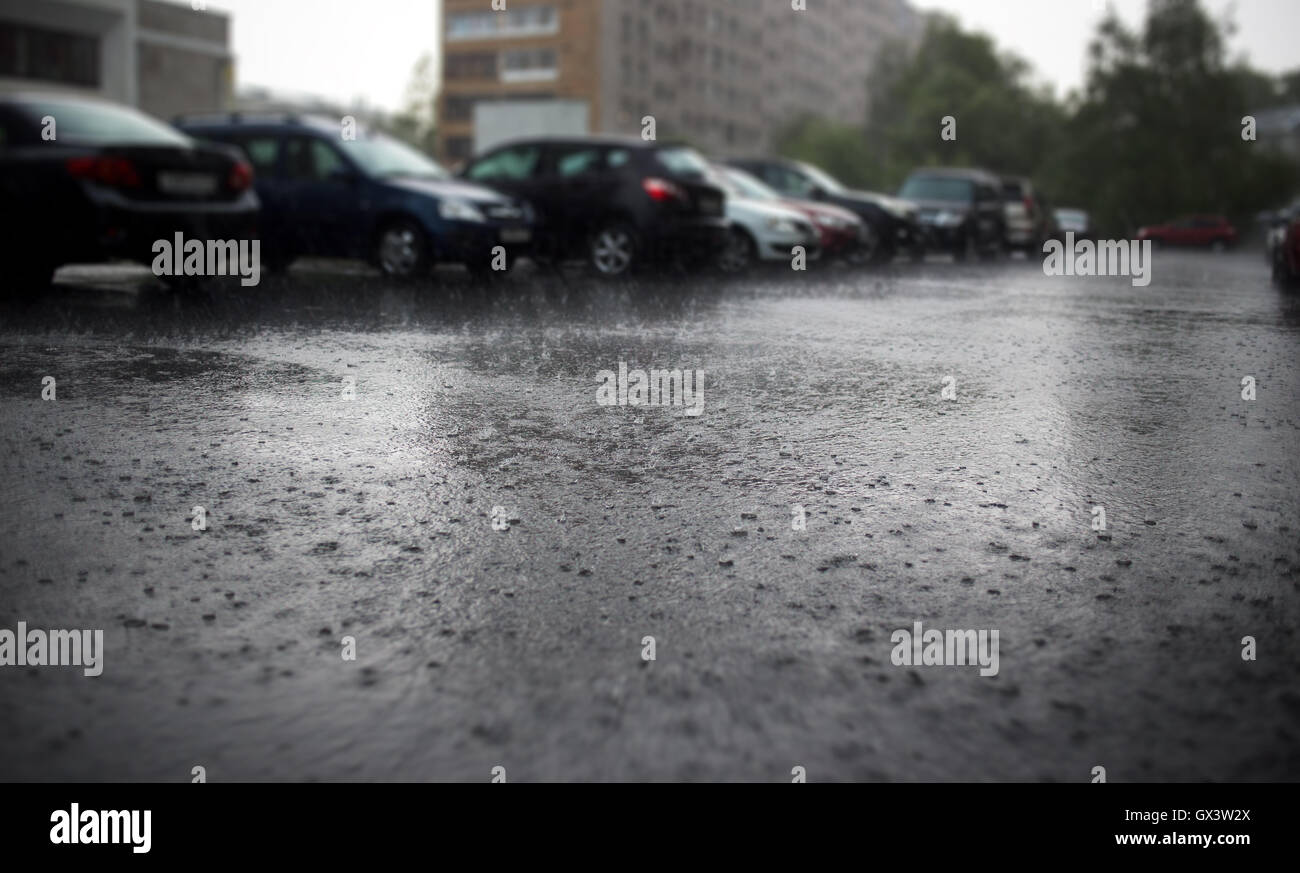 Heavy rain on city street with parked cars at background. Stock Photo