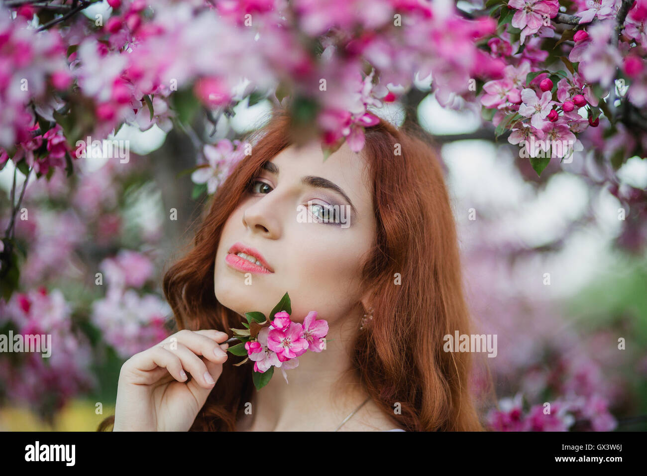 Closeup portrait of beautiful female hold blossom branch  in fresh pink floral garden, warm sunset light, spring nature, vacation and leisure concept Stock Photo