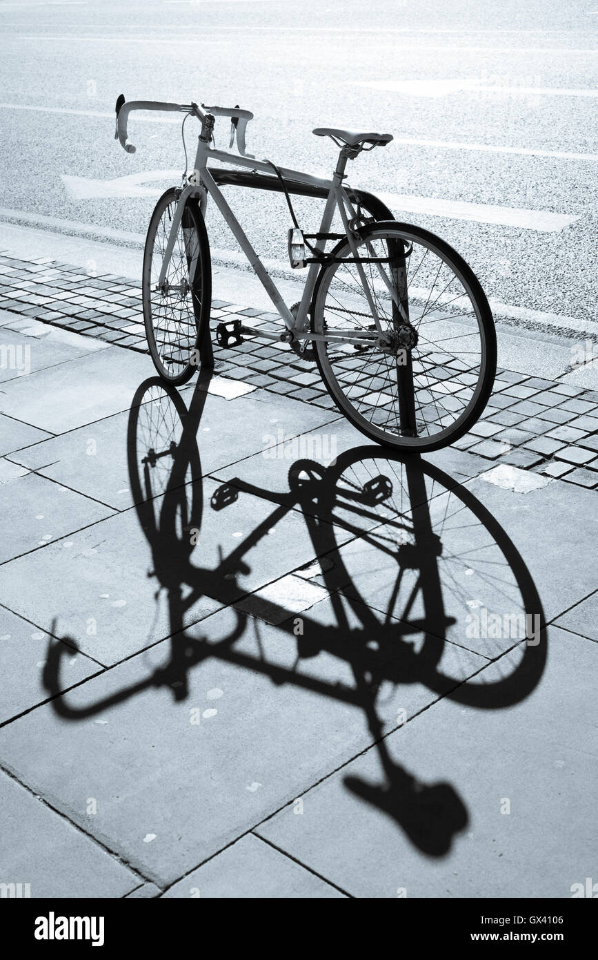 Hipster single gear fixie bicycle locked to a metal stand on a pavement. Big shadow projected on the pavement. Stock Photo