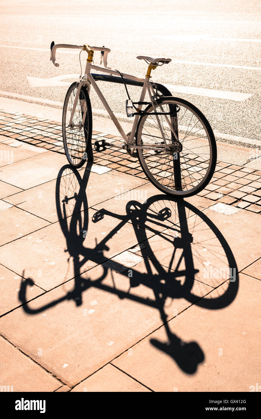 Hipster single gear fixie bicycle locked to a metal stand on a pavement. Big shadow projected on the pavement. Instagram effect. Stock Photo