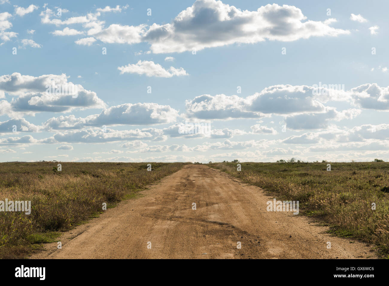 Unsealed dirt road with clouds and blue sky background Stock Photo