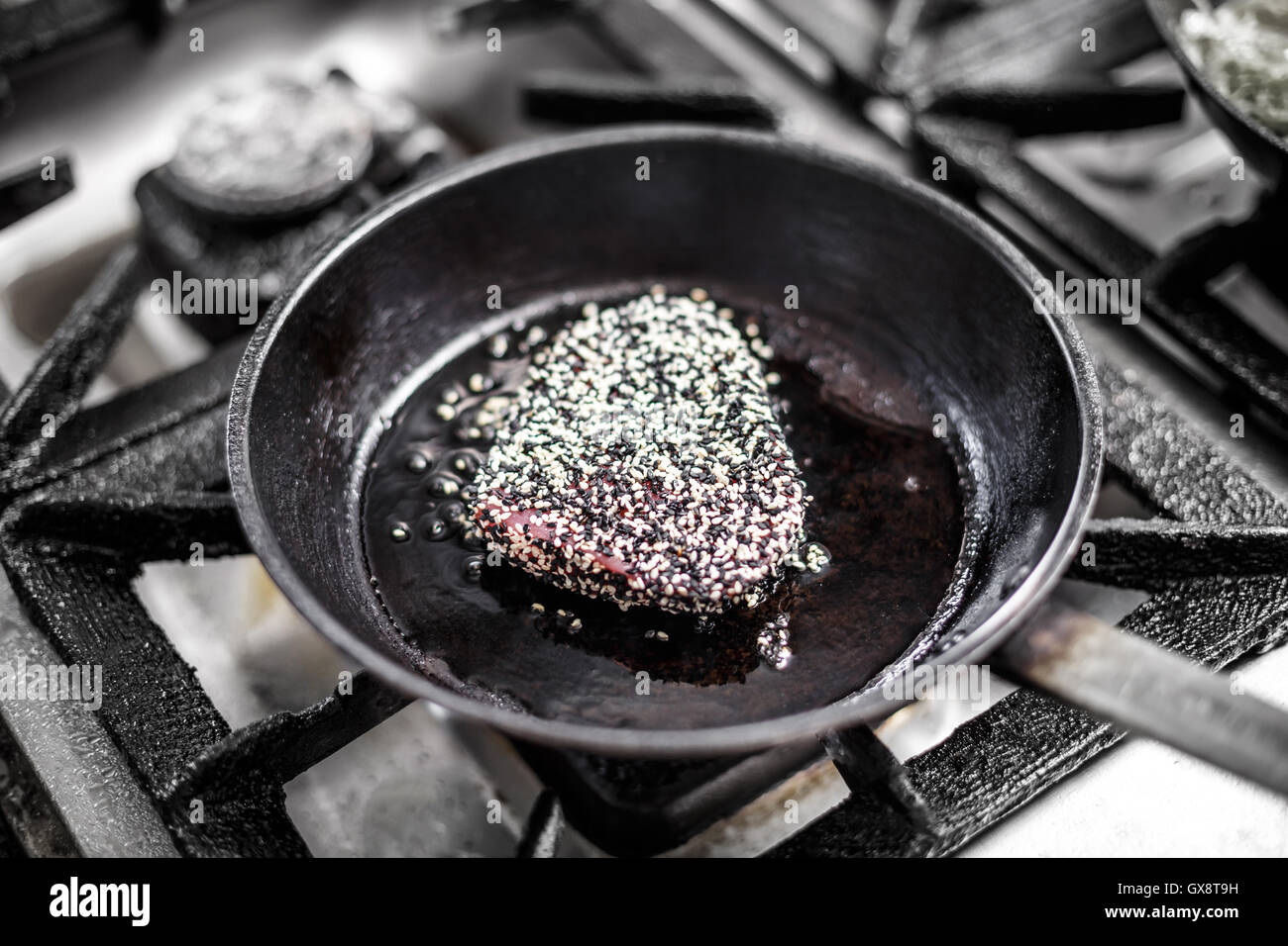 Red tuna steak crusted with white and black sesame seeds being fried on olive oil on pan Stock Photo