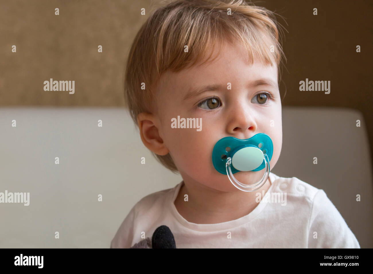 Baby with dummy in his mouth sitting on the bed in the room Stock Photo