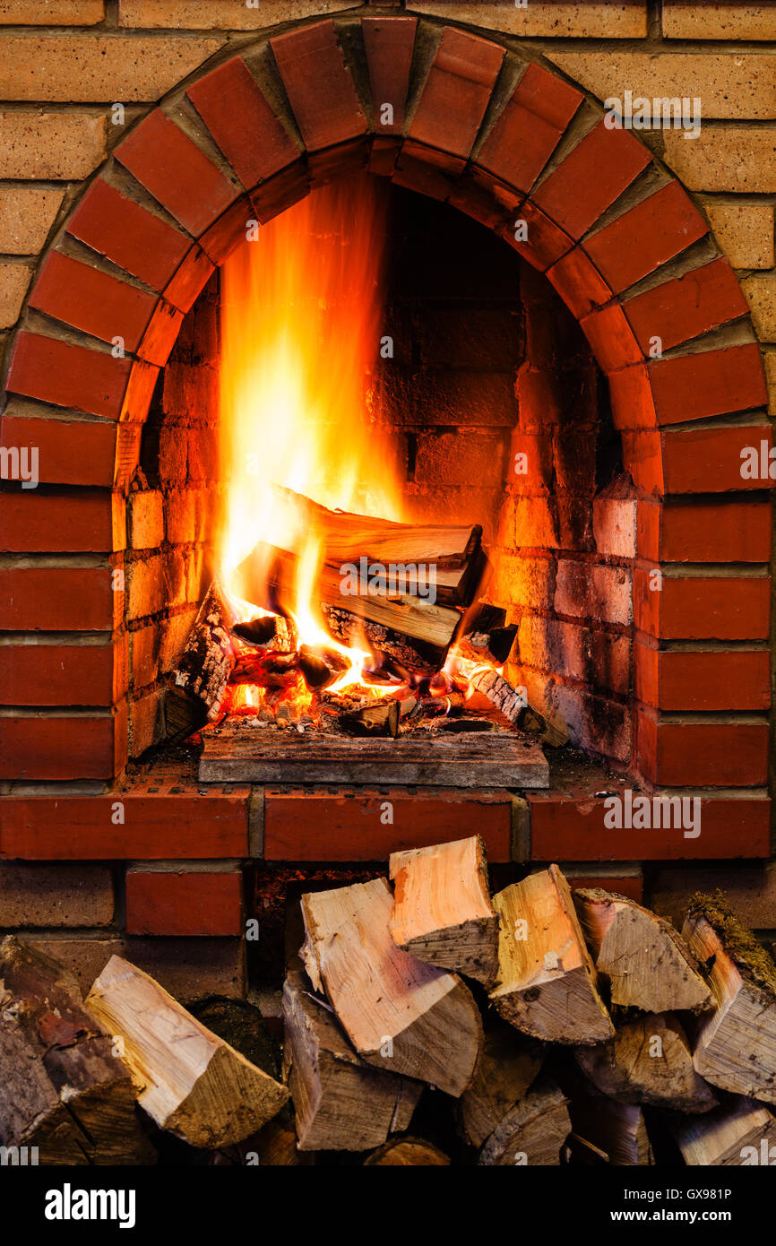 pile of firewood and firewood burning in indoor brick fireplace in country cottage Stock Photo