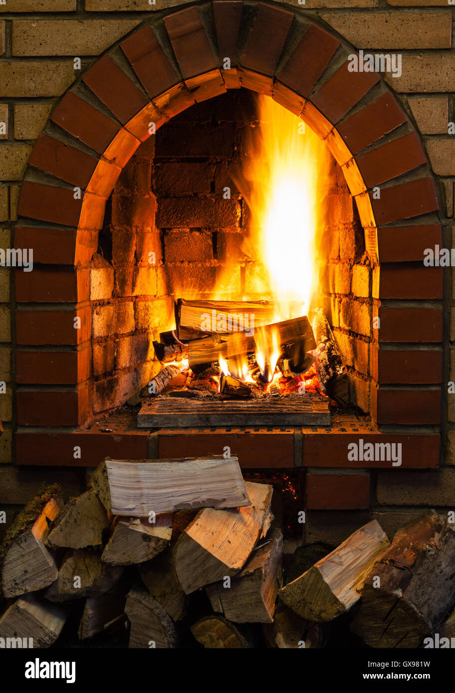 pile of wood and logs burning in indoor brick fireplace in country cottage Stock Photo