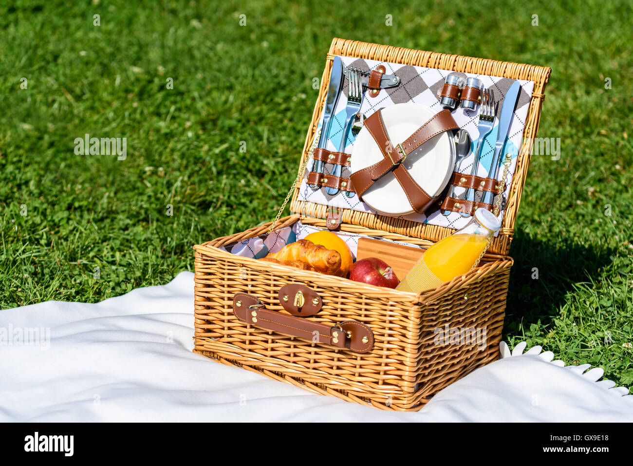 Picnic Basket Food On White Blanket With Pillows In Summer Stock Photo