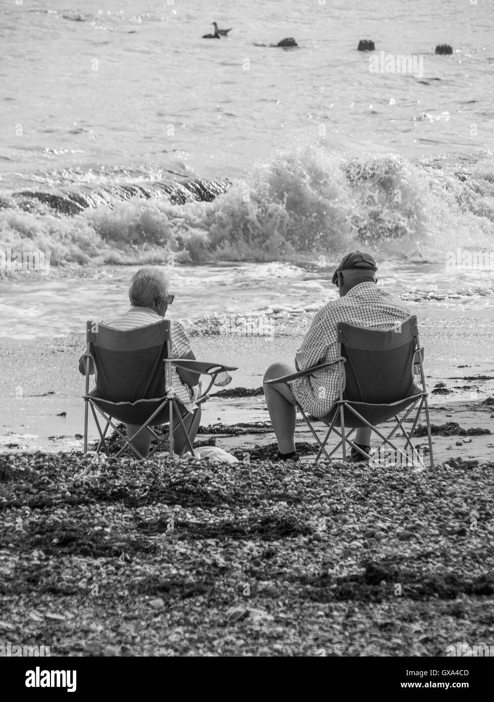 Elderly Couple sitting on beach Stock Photo