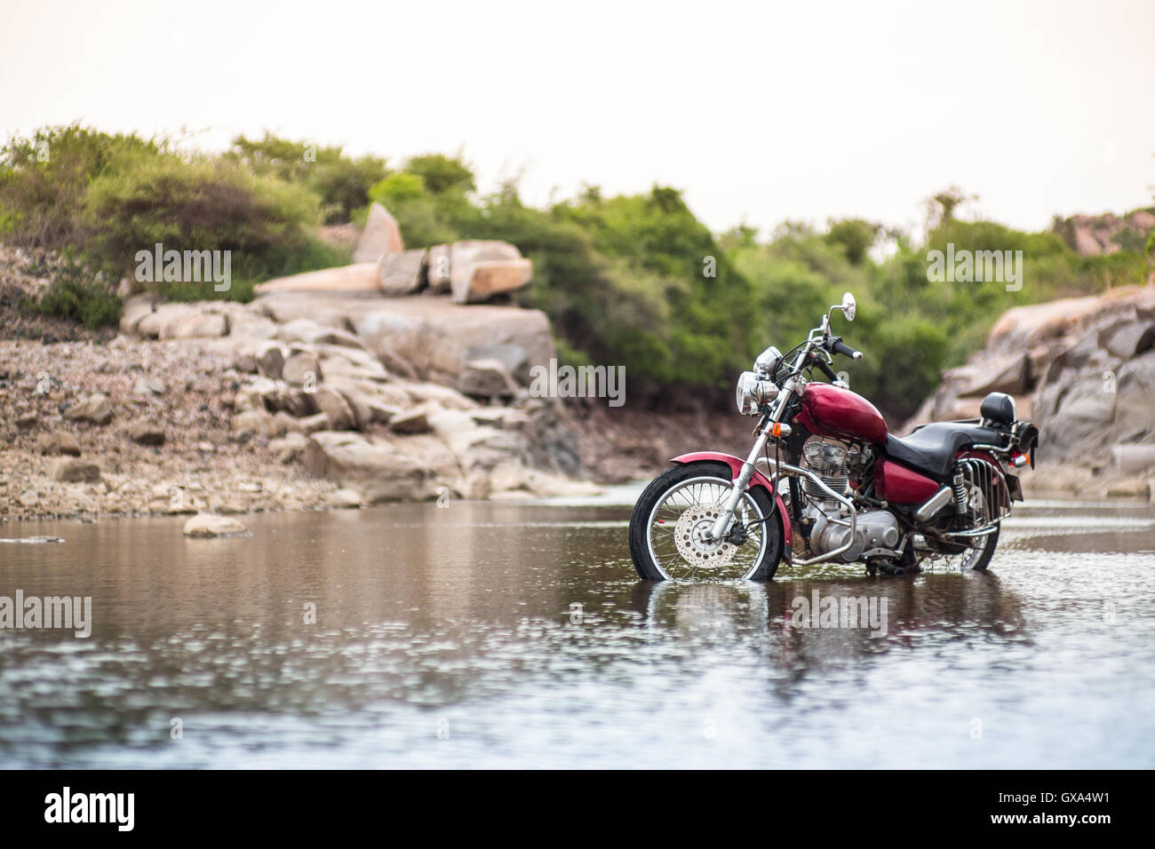A red motorcycle standing in shallow waters of a river in the sunset ...