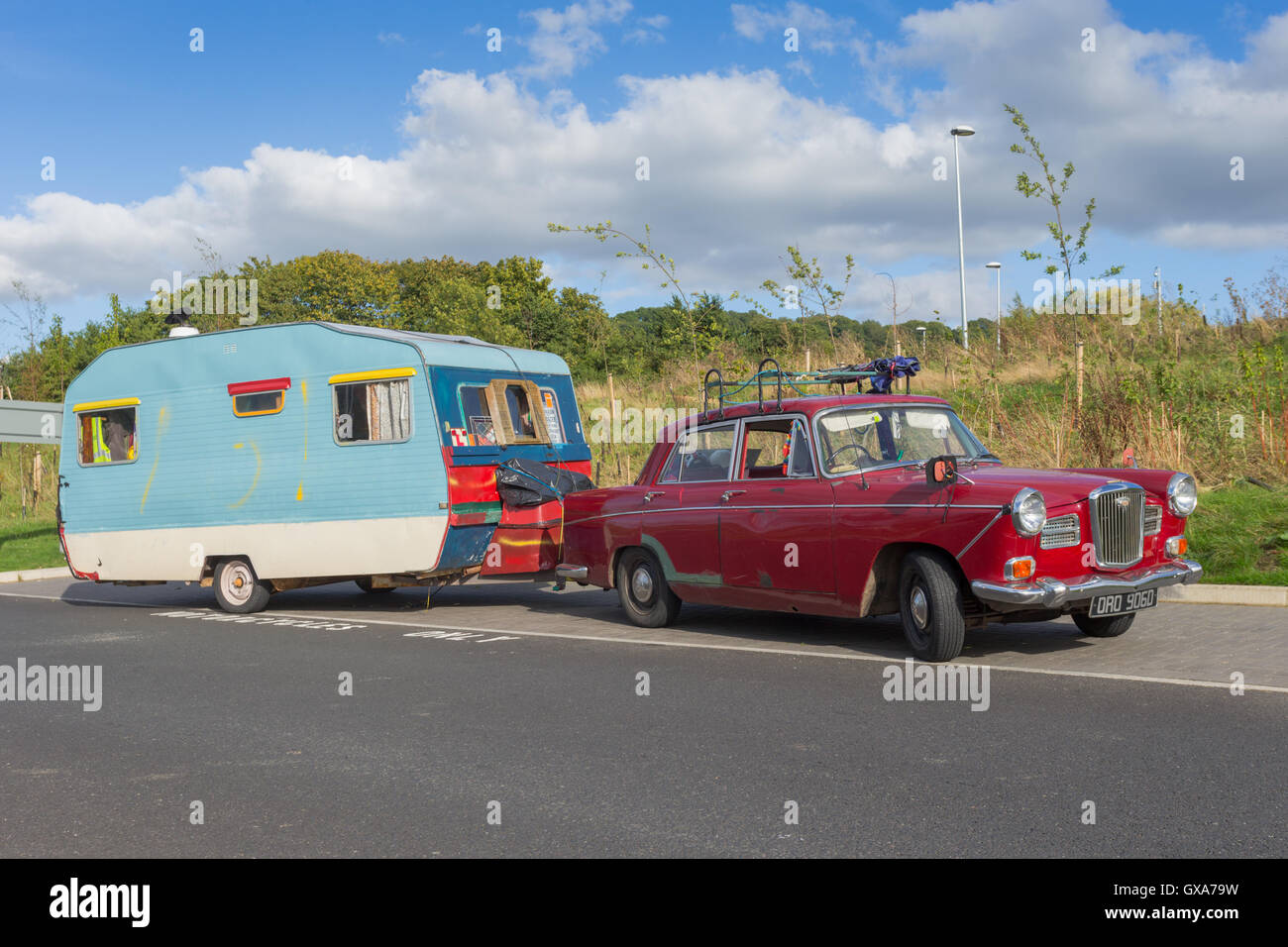 Tradition caravan trailer from the 1960s being towed by an old car from the same period, parked at a motorway services Stock Photo