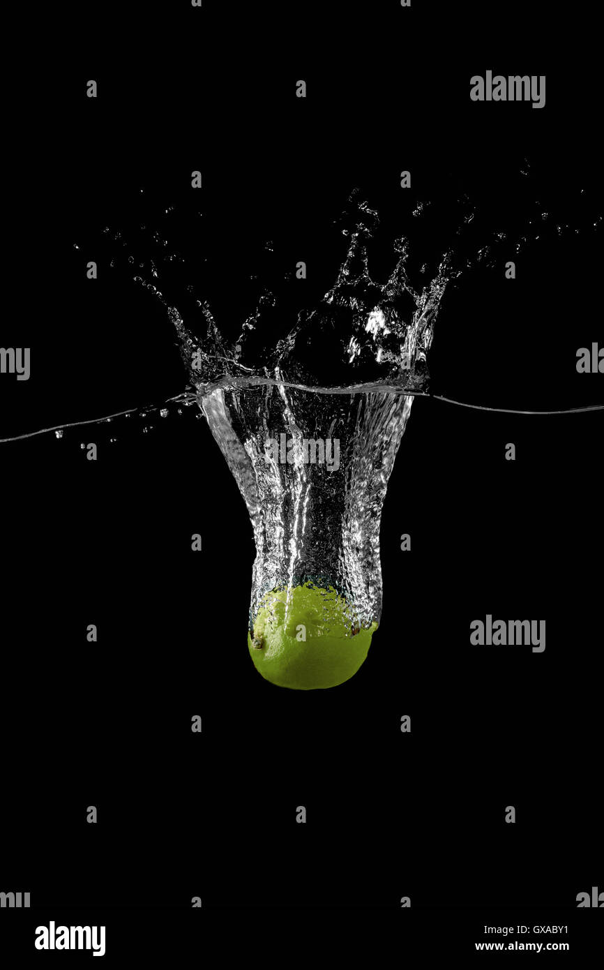 lime are falling into the water holding up a lot of splashes on a dark background Stock Photo