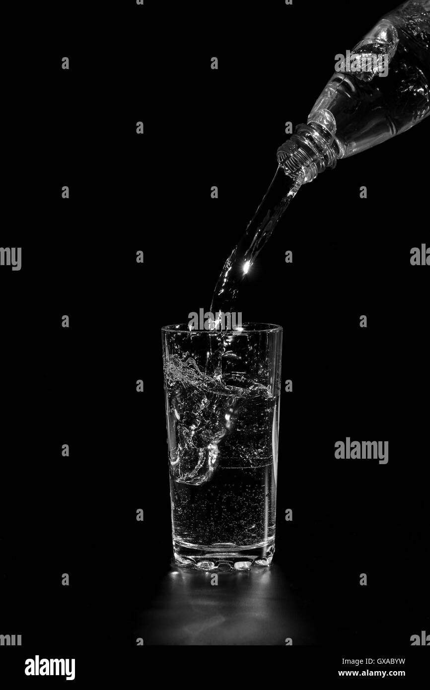 Mineral water is poured into a glass from a bottle in the dark Stock Photo