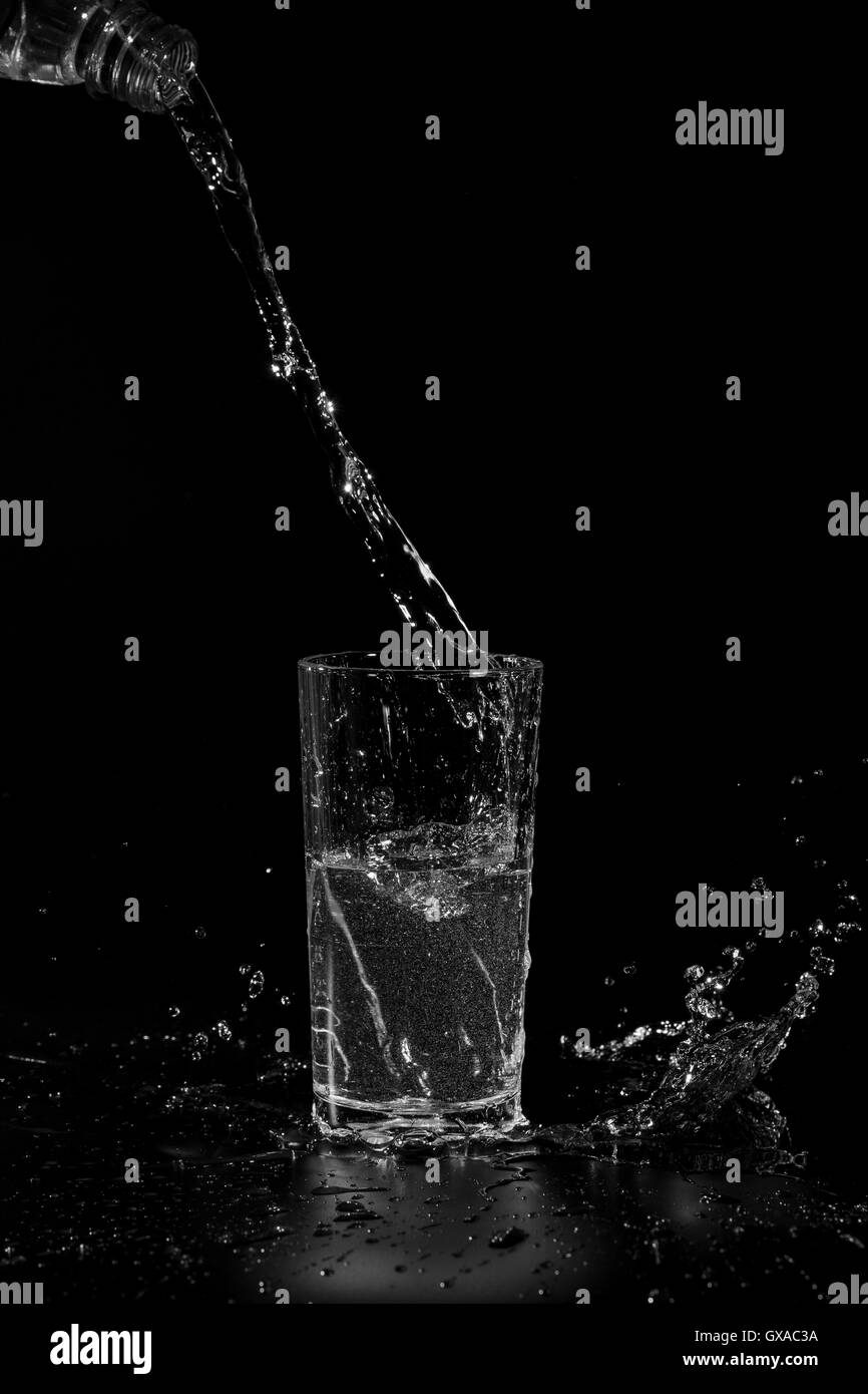 Water poured from the bottle into a transparent glass beaker on a black background Stock Photo