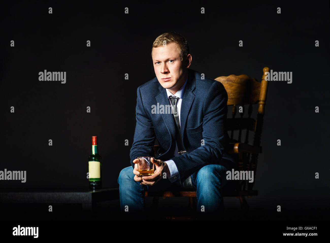 Portrait serious elegant handsome young man in suit toasting with glass of alcohol on black background. Stock Photo