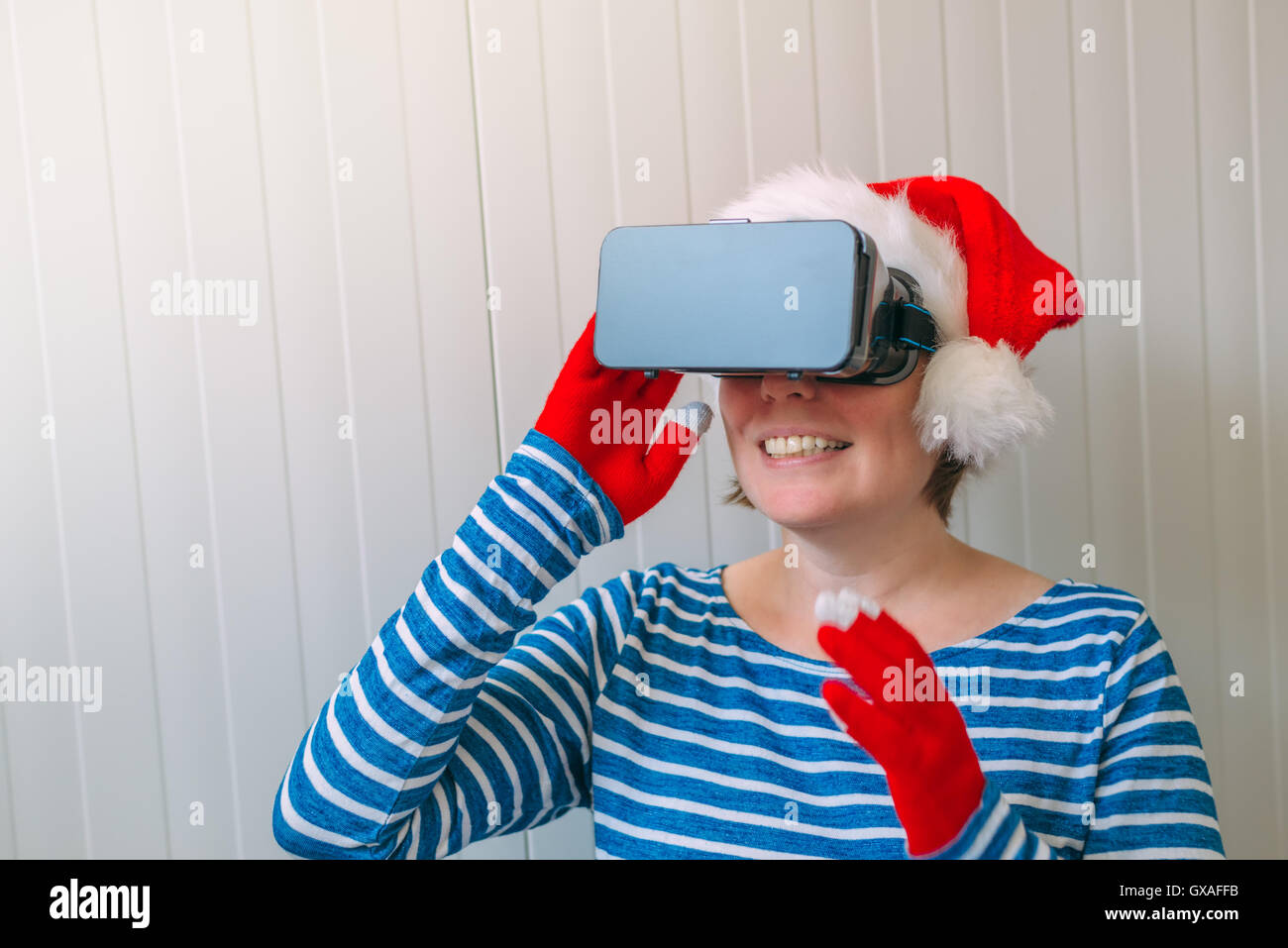 Woman with Christmas Santa Claus hat and VR headset goggles enjoying 360 view video and virtual reality multimedia content. Stock Photo