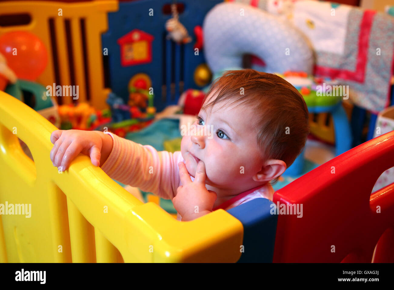 Baby girl thinking in a colourful playpen Stock Photo