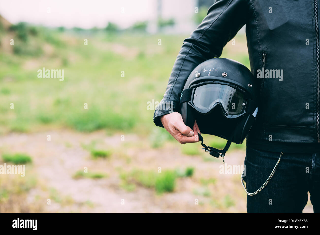 Mid section of male motorcyclist standing on wasteland holding helmet Stock Photo