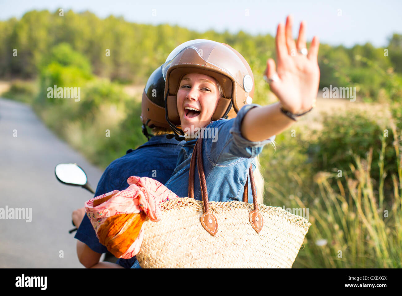 Young woman riding pillion on rural road waving, Majorca, Spain Stock Photo