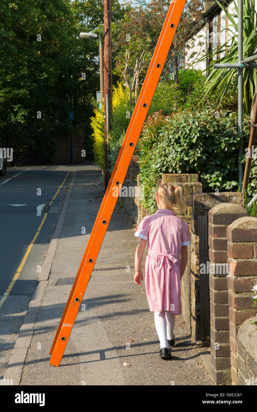 Pedestrian / young school girl / kid / child in uniform / people / person walking under scaffolding ladder, risking bad luck. UK Stock Photo