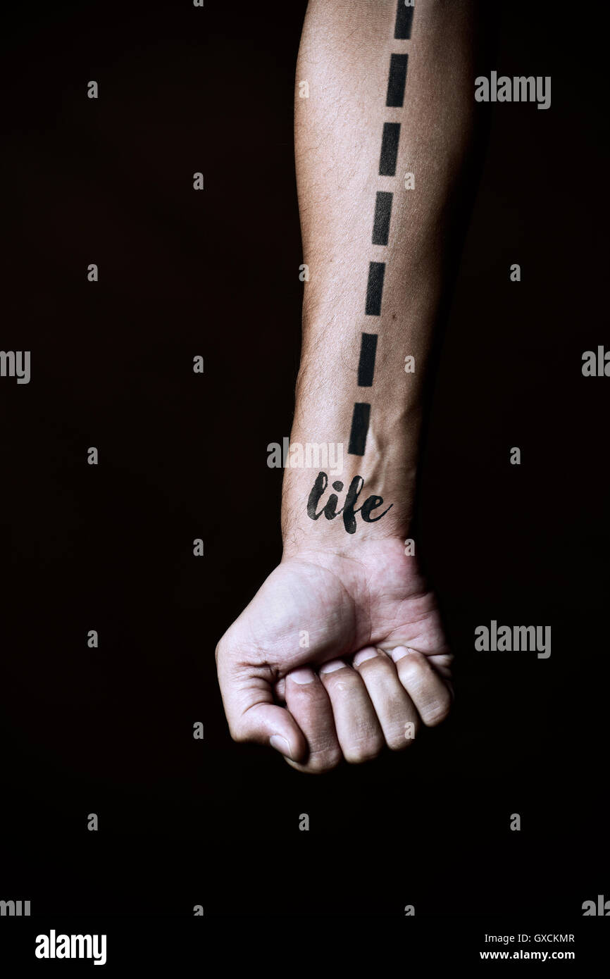 closeup of a young caucasian man with a dashed line and the word life simulating a tattoo in his forearm, against a black backgr Stock Photo
