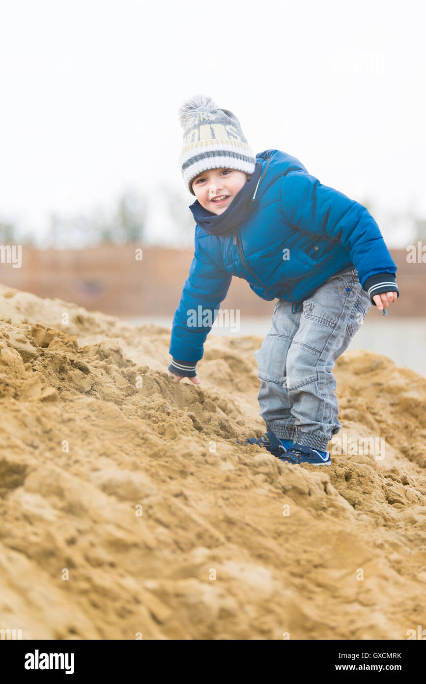 child climbing on a pile of sand in Winter Beach Stock Photo