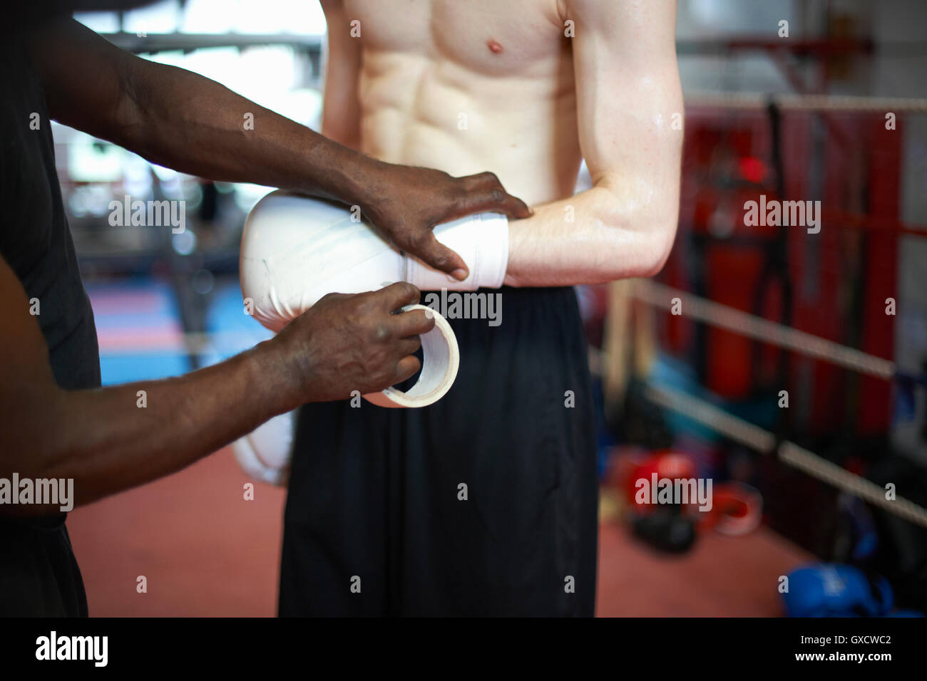 Coach helping boxer put on gloves, mid section Stock Photo