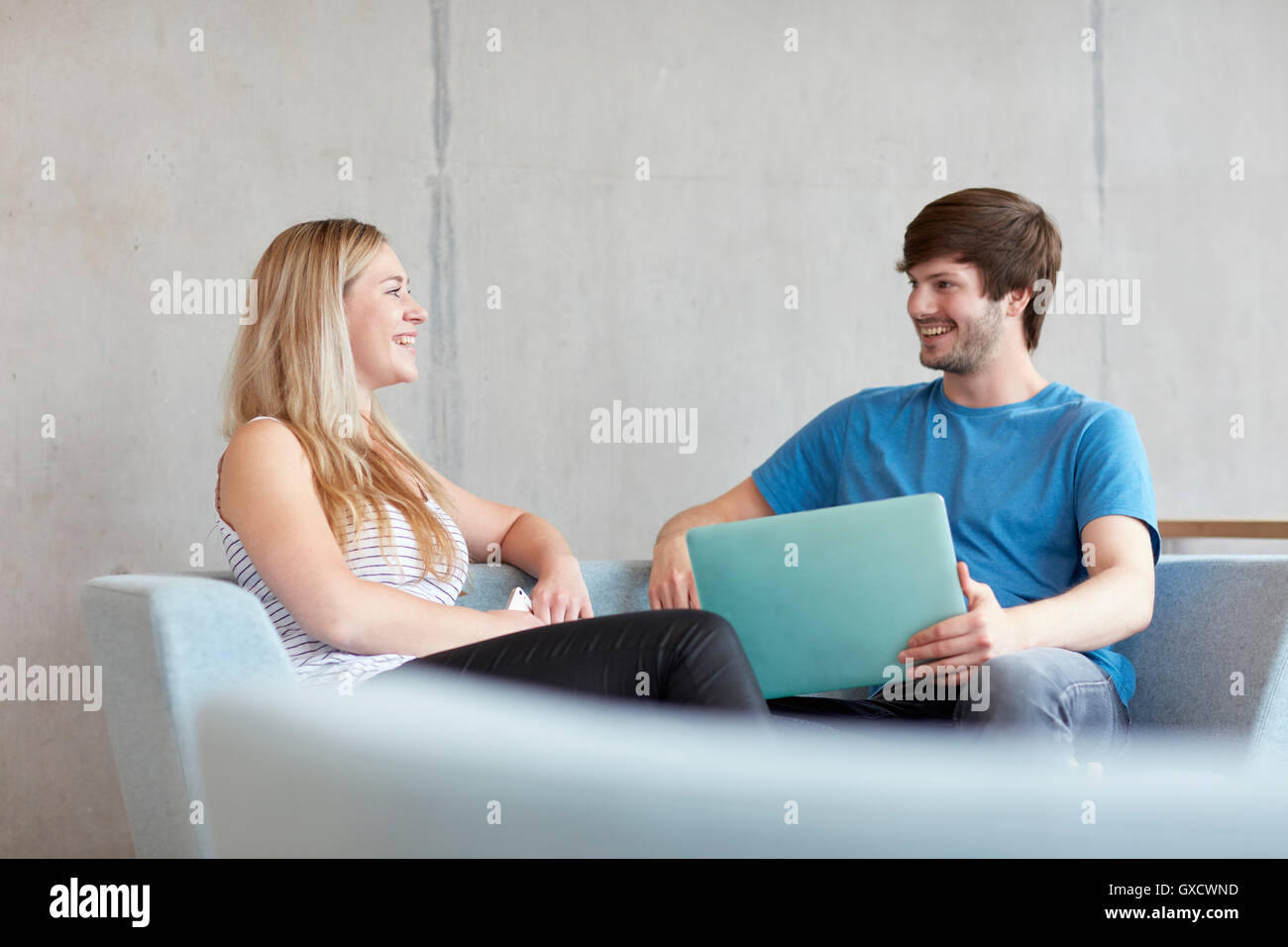 Young male and female students sitting on study space sofa with laptop at higher education college Stock Photo