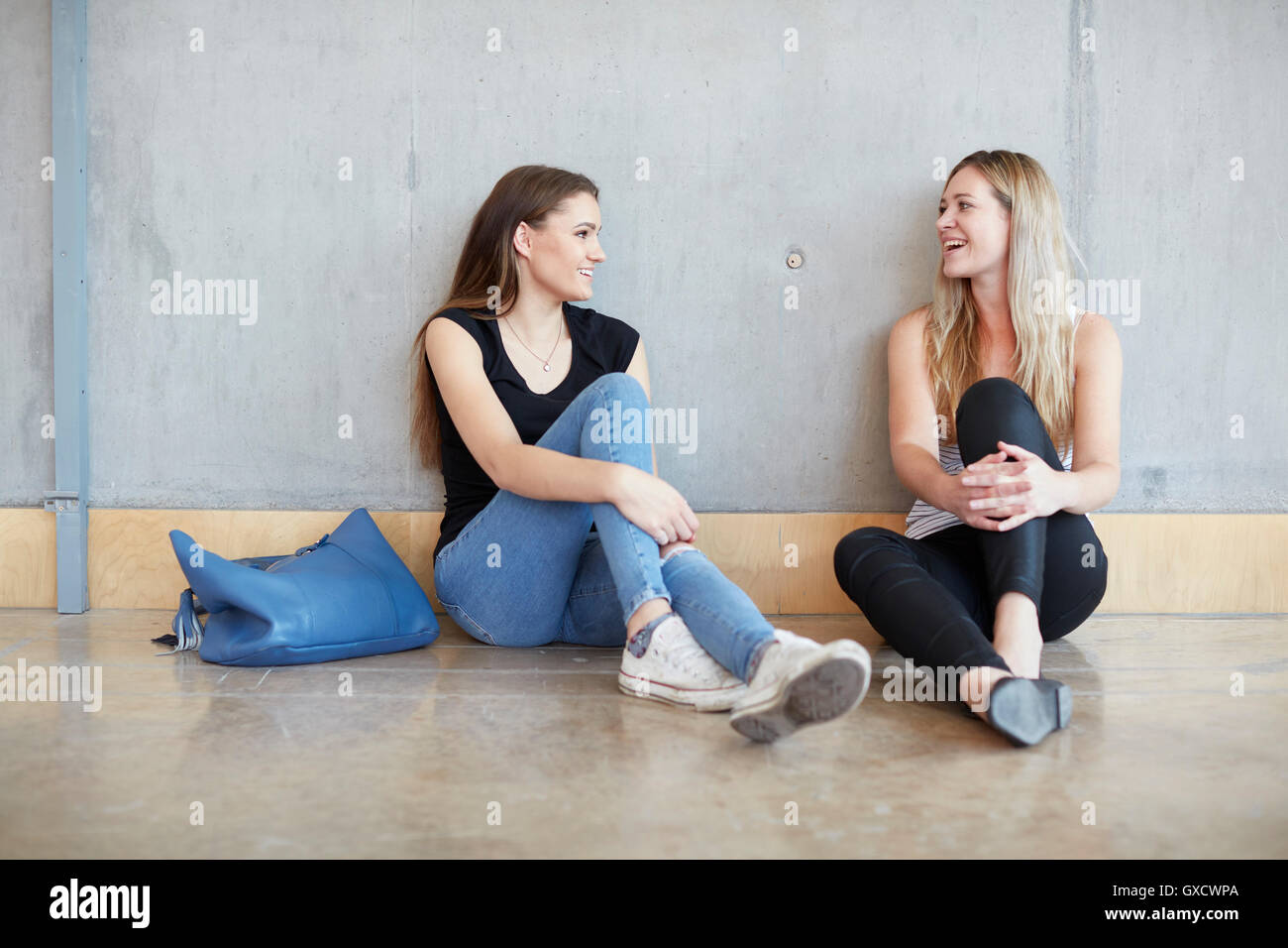 Two young female students sitting on floor chatting at higher education college Stock Photo