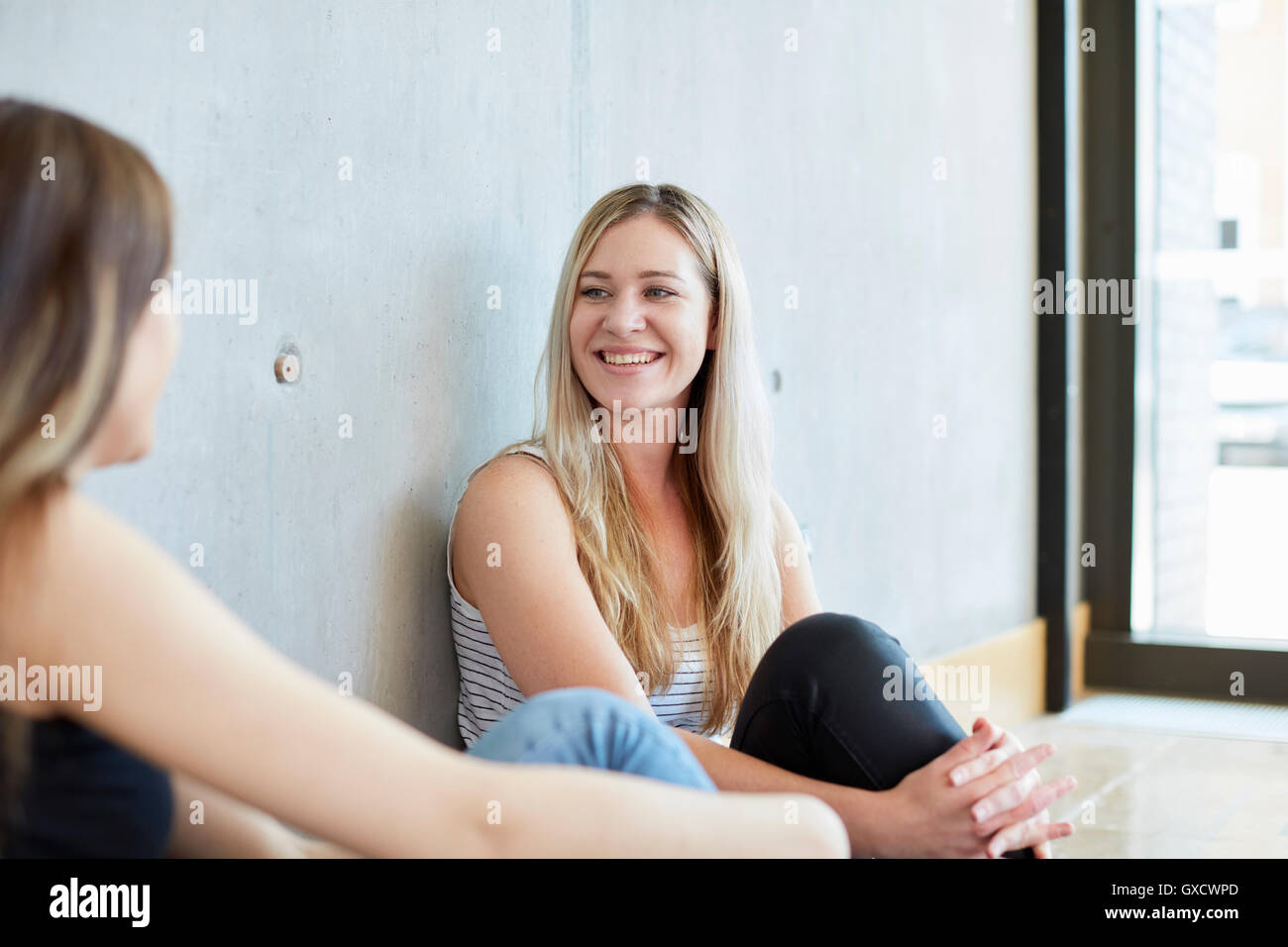 Two young female students sitting on floor chatting at higher education college Stock Photo
