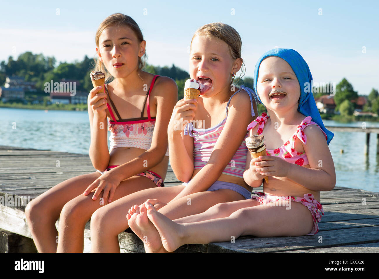 Two sisters and female toddler on pier eating ice cream cones, Lake Seeoner See, Bavaria, Germany Stock Photo