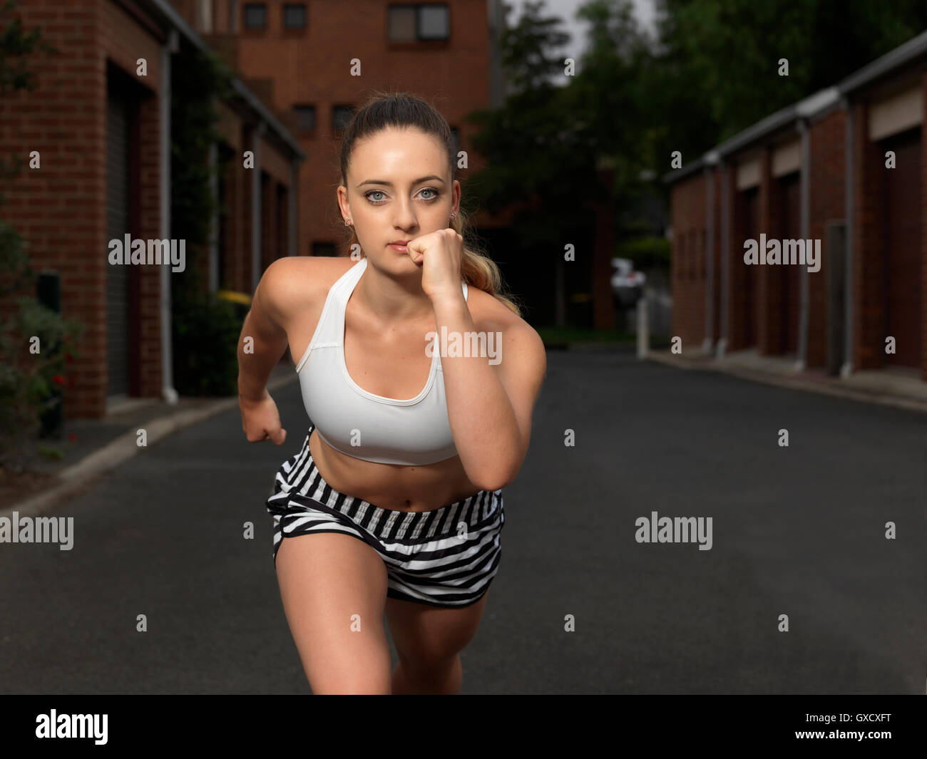 Portrait of young female runner poised to run on urban street Stock Photo
