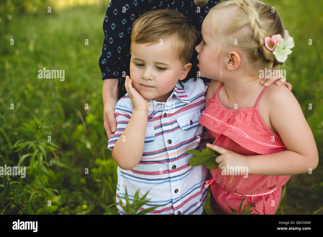 Girl whispering in brothers ear in meadow Stock Photo