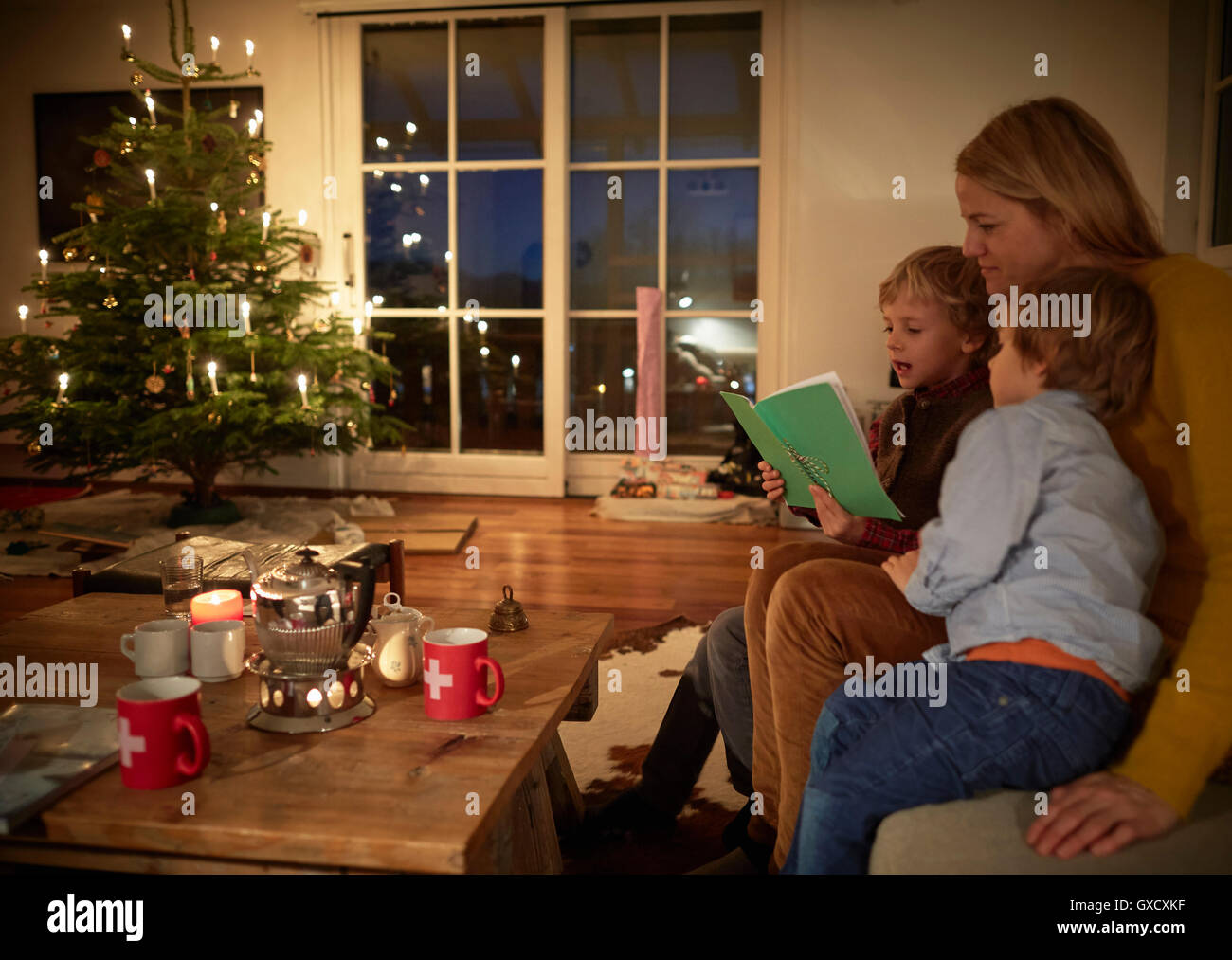 Mother and sons sitting at home at Christmas, reading book Stock Photo