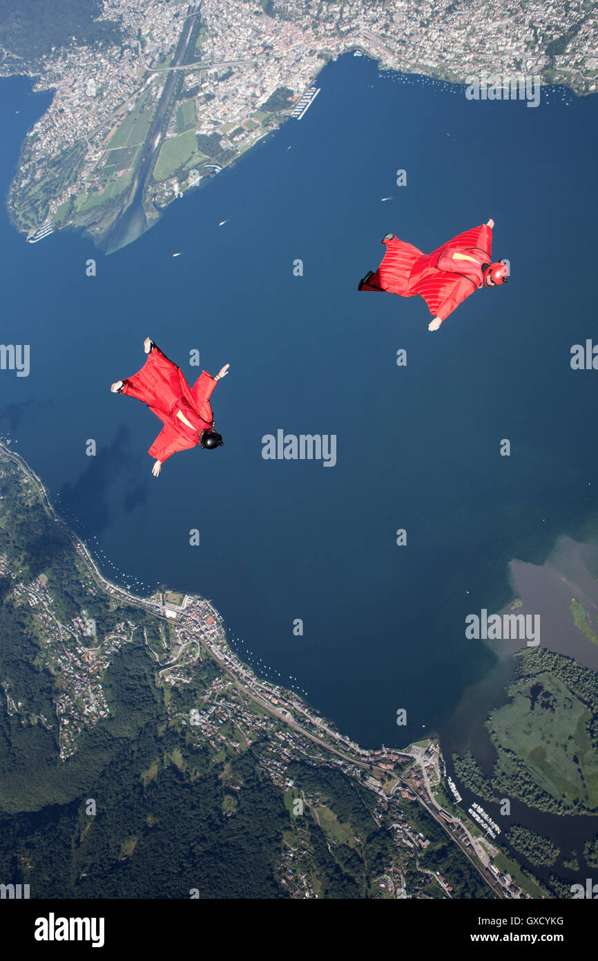 Two wingsuit skydiver pilots team training and flying close together over lake, Locarno, Tessin, Switzerland Stock Photo