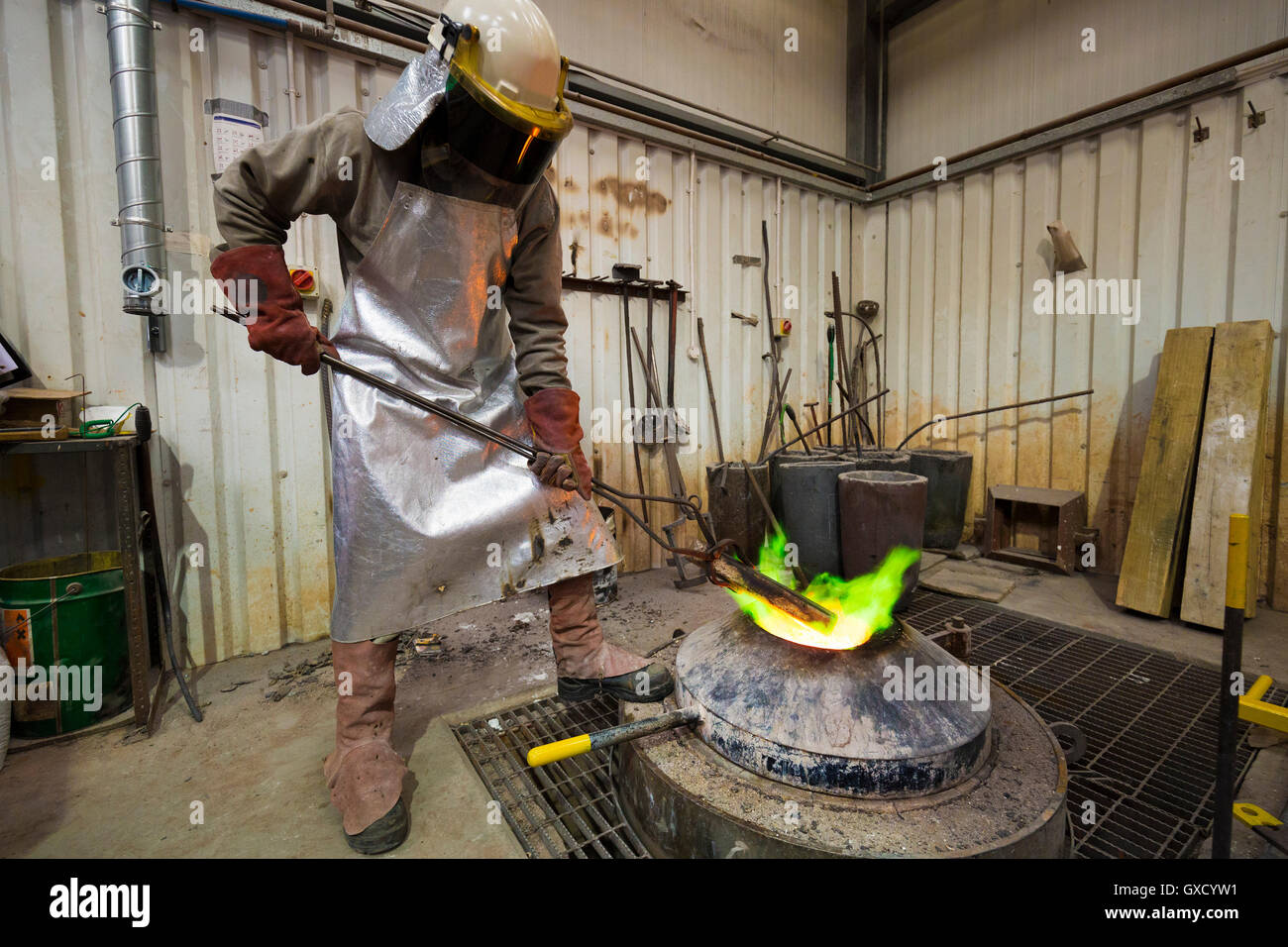 Male foundry worker heating bronze ingot over furnace in bronze foundry