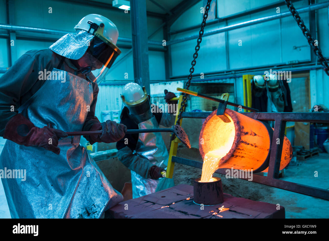 Male foundry workers pouring bronze melting pot in bronze foundry Stock Photo
