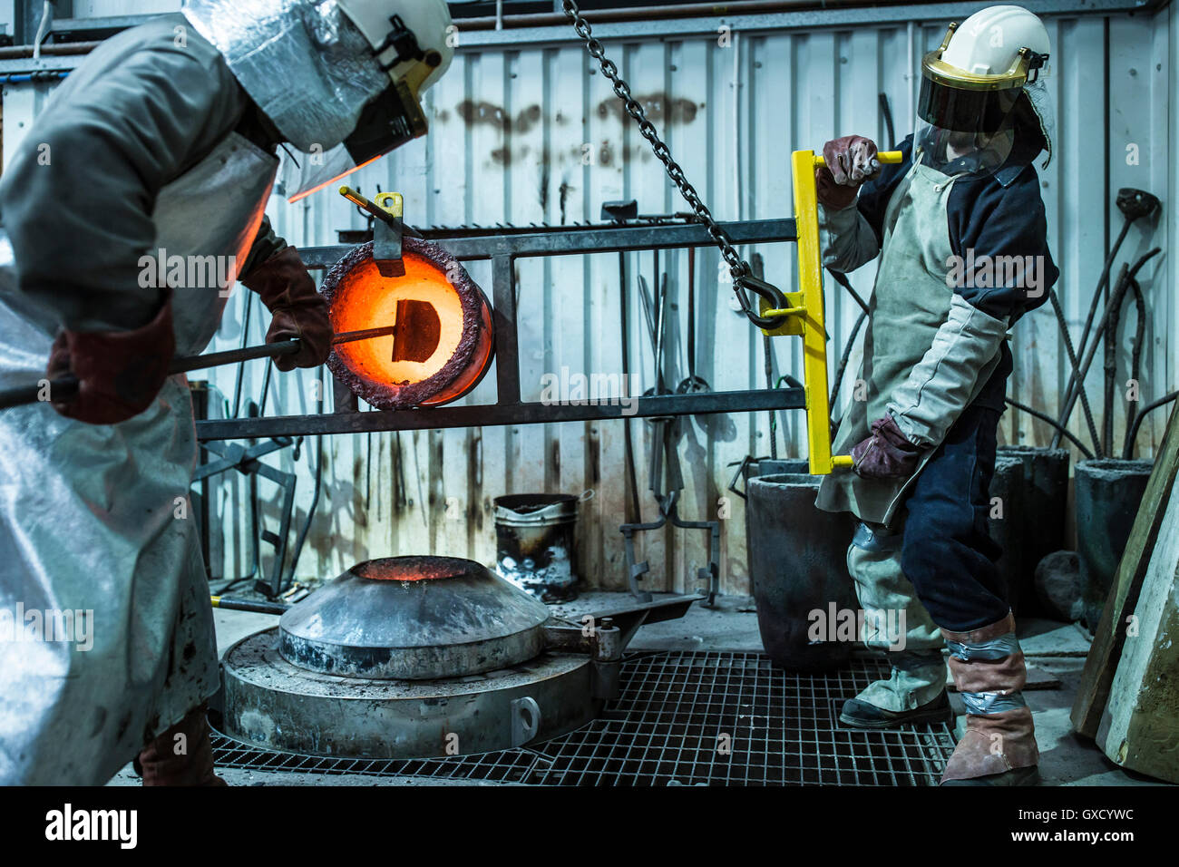 Male foundry worker working with bronze melting pot in bronze foundry