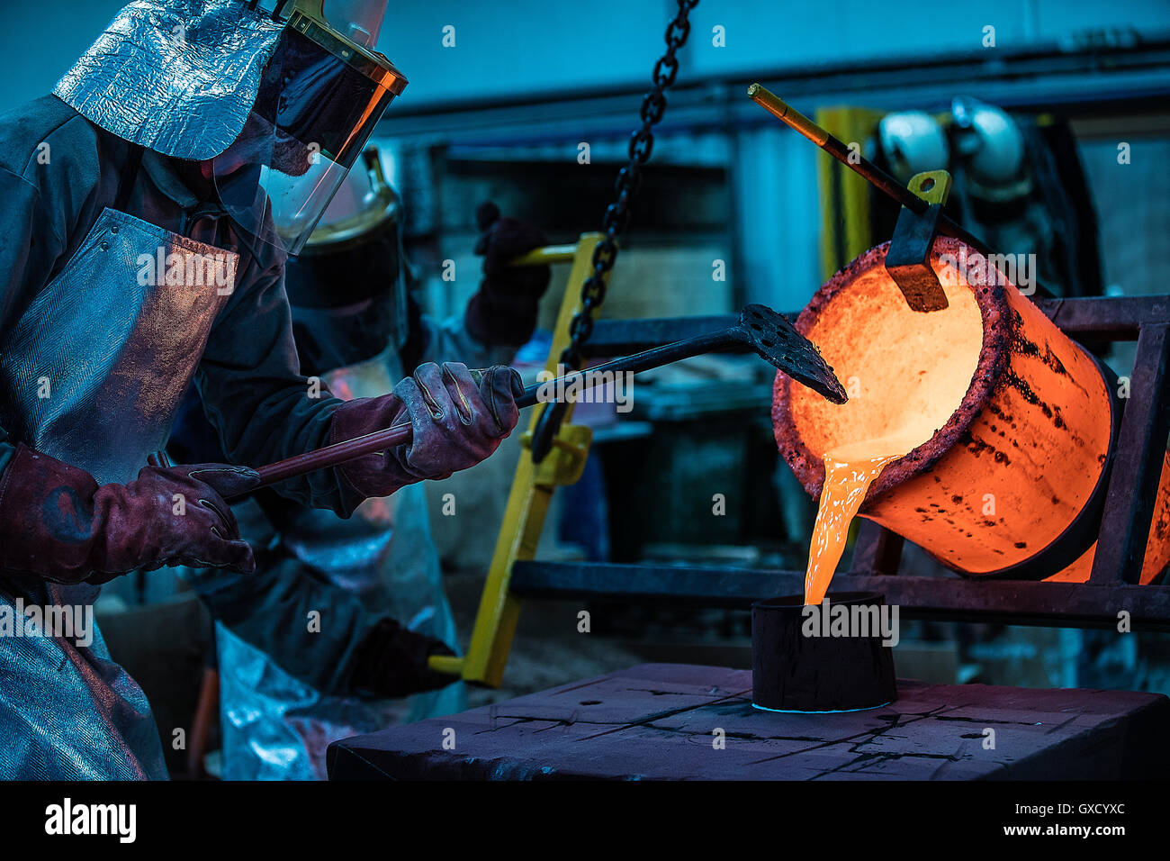 Male foundry workers pouring bronze melting pot in bronze foundry Stock