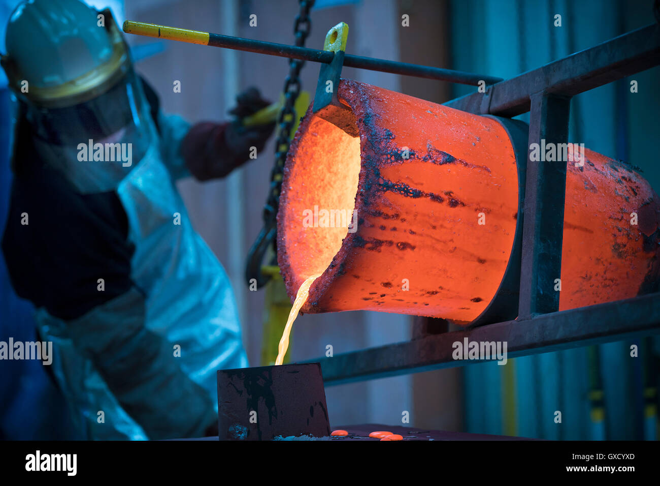 Male foundry worker pouring bronze melting pot in bronze foundry Stock