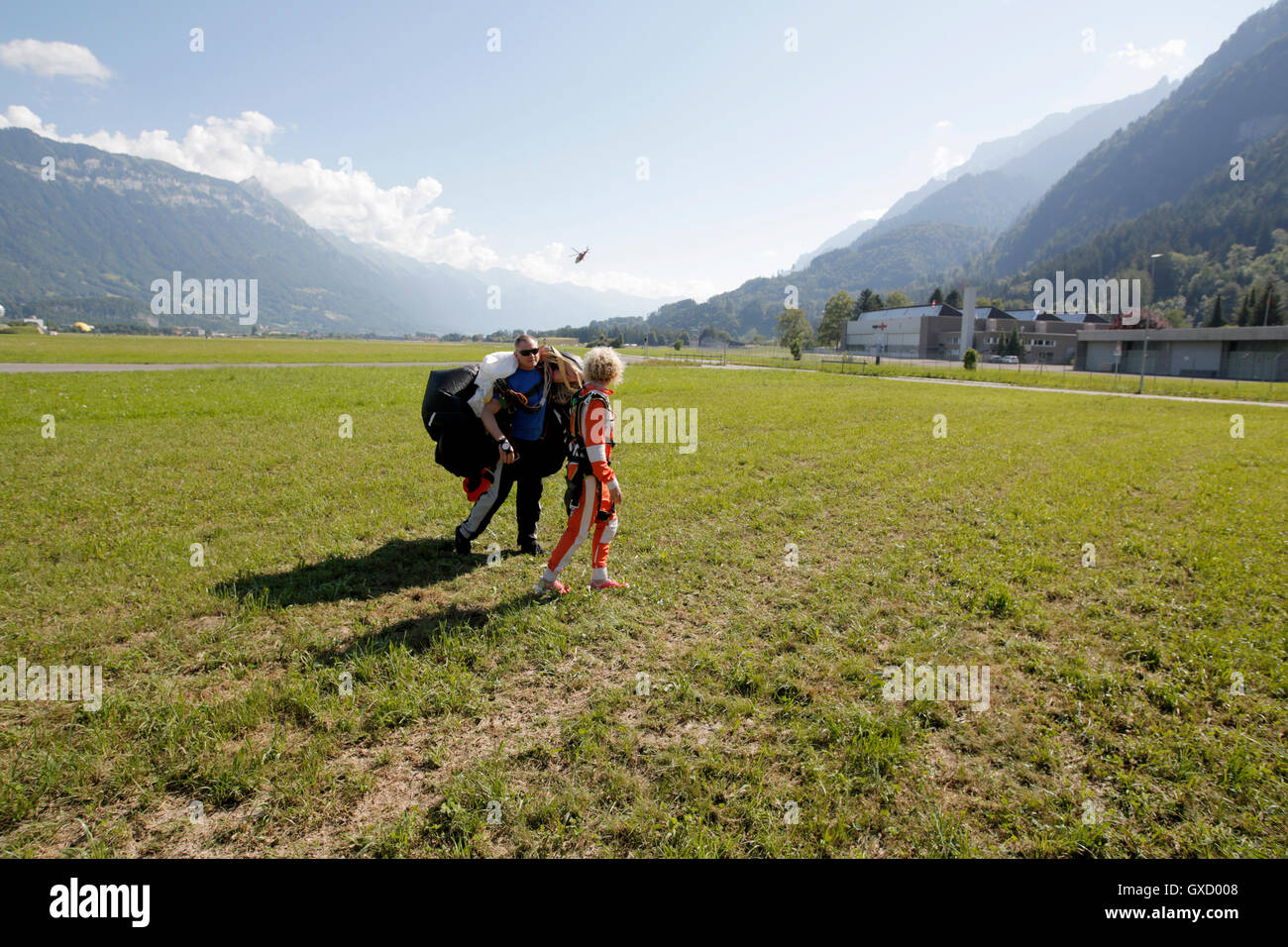 Tandem sky divers walking in field after landing, Interlaken, Berne, Switzerland Stock Photo