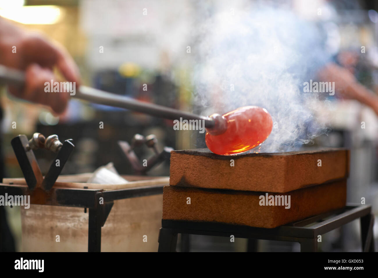 Molten glass material being shaped on blowpipe in workshop Stock Photo