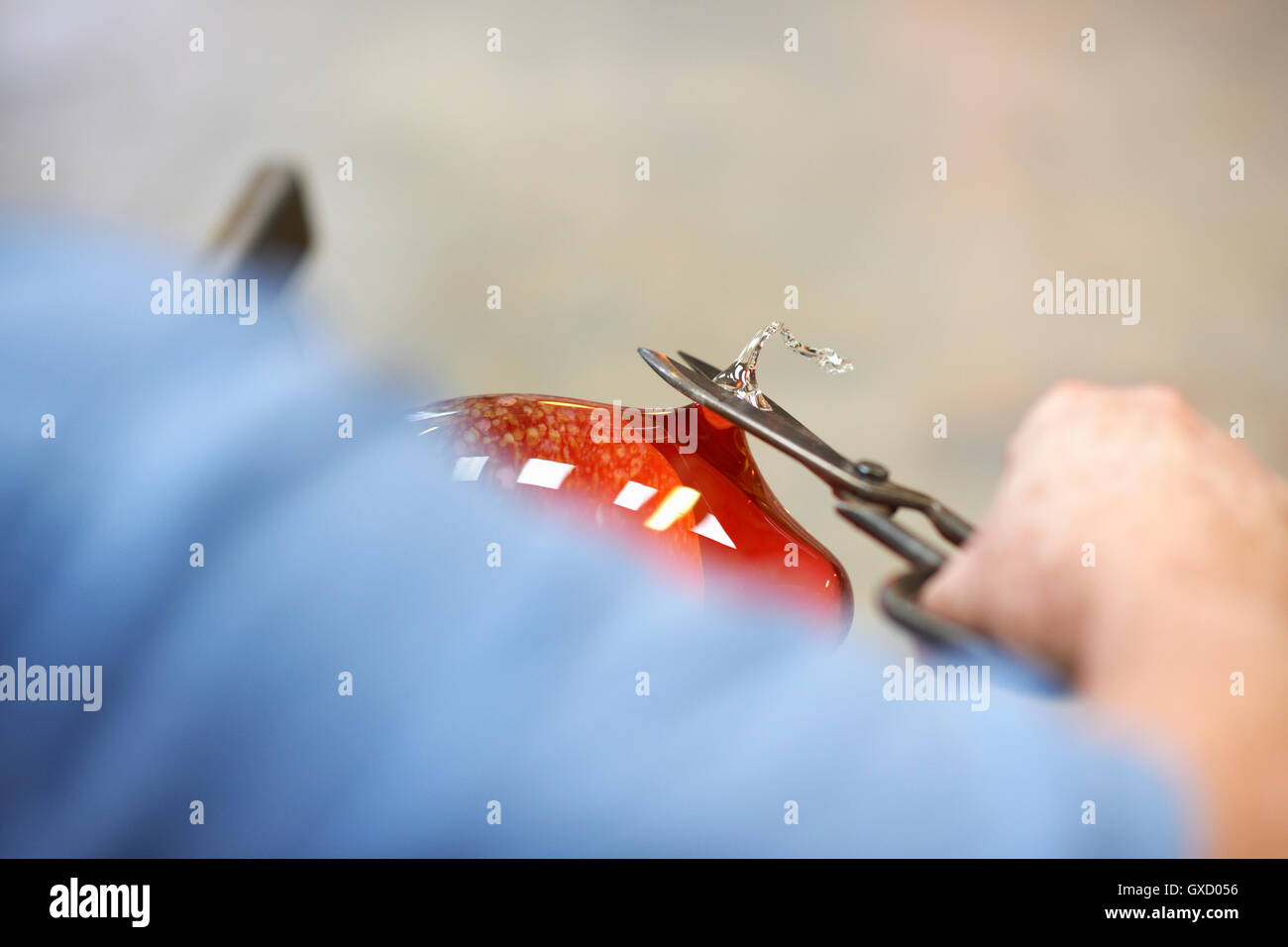 Glassblower in workshop shaping molten glass material with hand tools Stock Photo